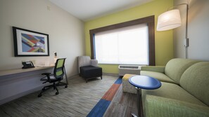 Quarto de hotel com escrivaninha, cadeira de escritório, sofá e uma janela grande com persianas.
