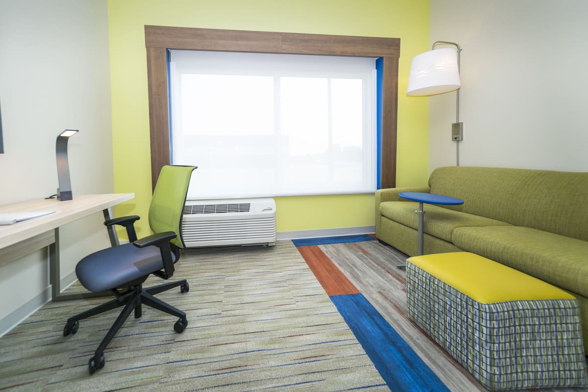 A room with a desk, chair, sofa, and a window.