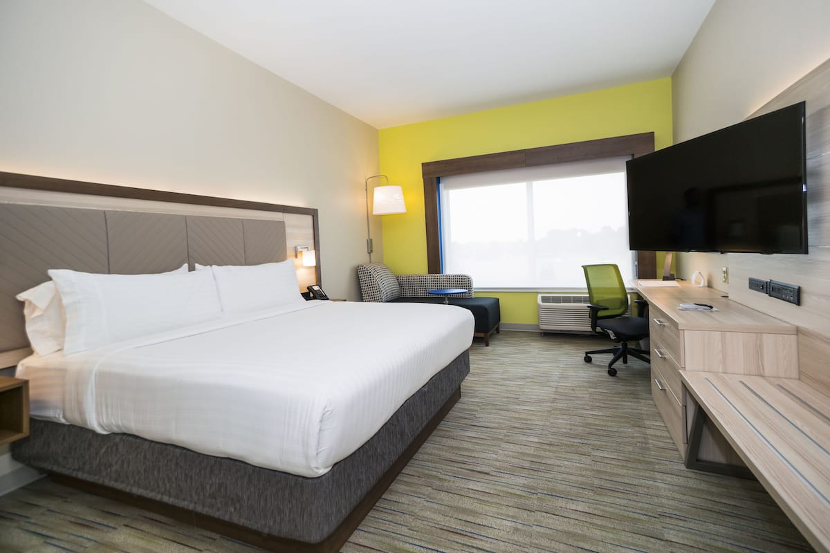 A hotel room with a bed, desk, chair, TV, and a window.
