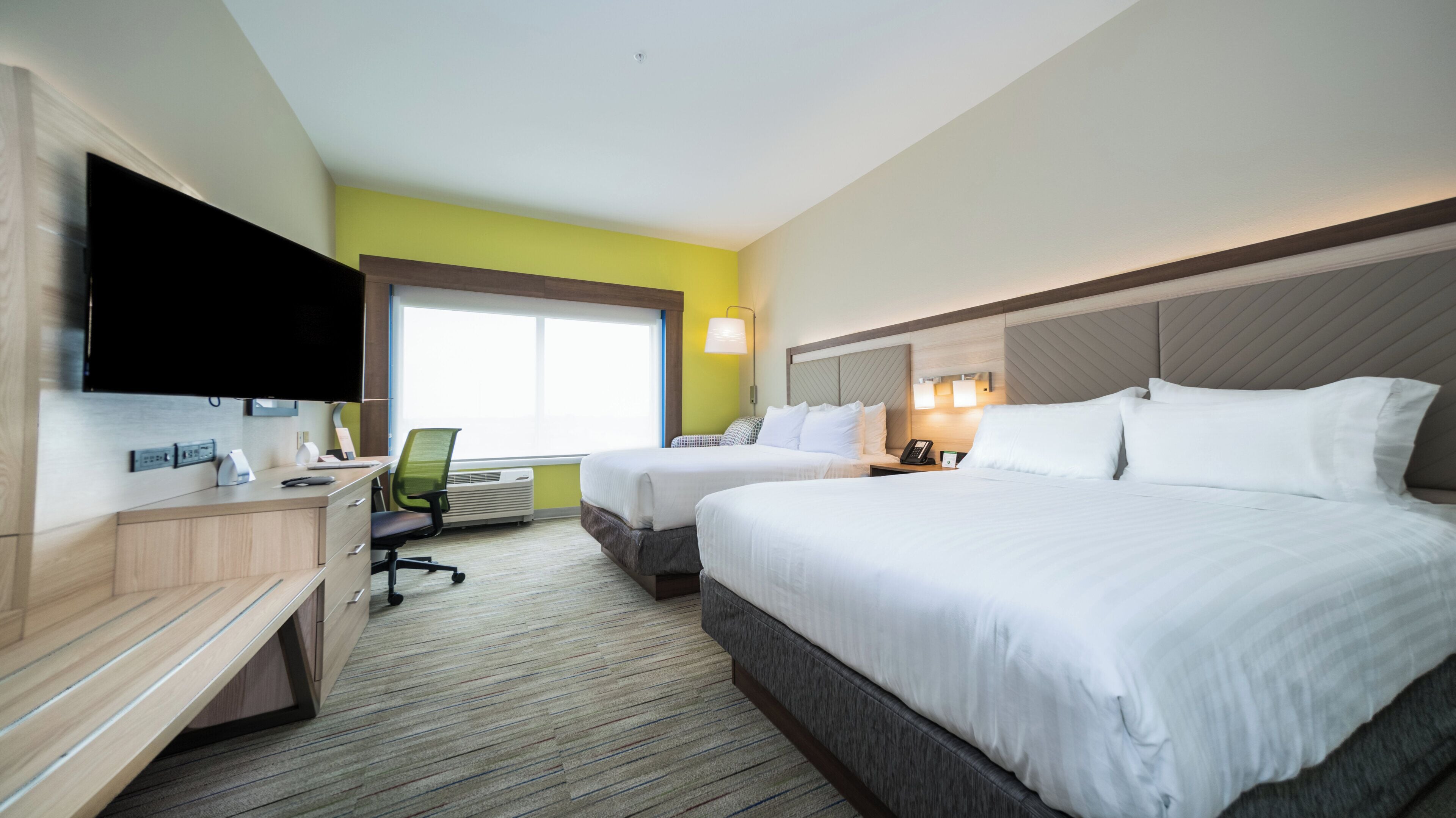 Une chambre d’hôtel avec deux lits, un bureau, une chaise, un téléviseur à écran plat, une fenêtre et une lampe fixée au mur.