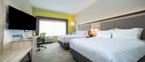 A hotel room with two beds, a desk, a chair, a flat-screen TV, a window, and a wall-mounted lamp.