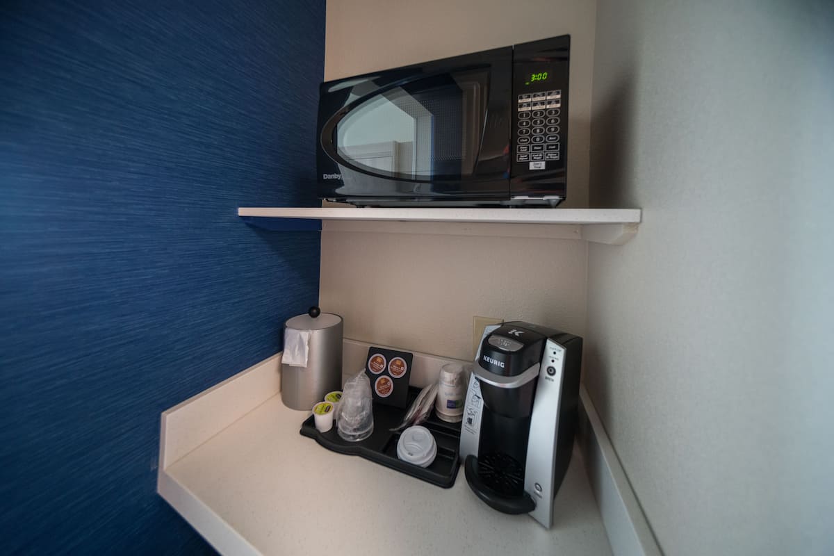 A kitchenette with a microwave, coffee maker, and a tray with cups and condiments.