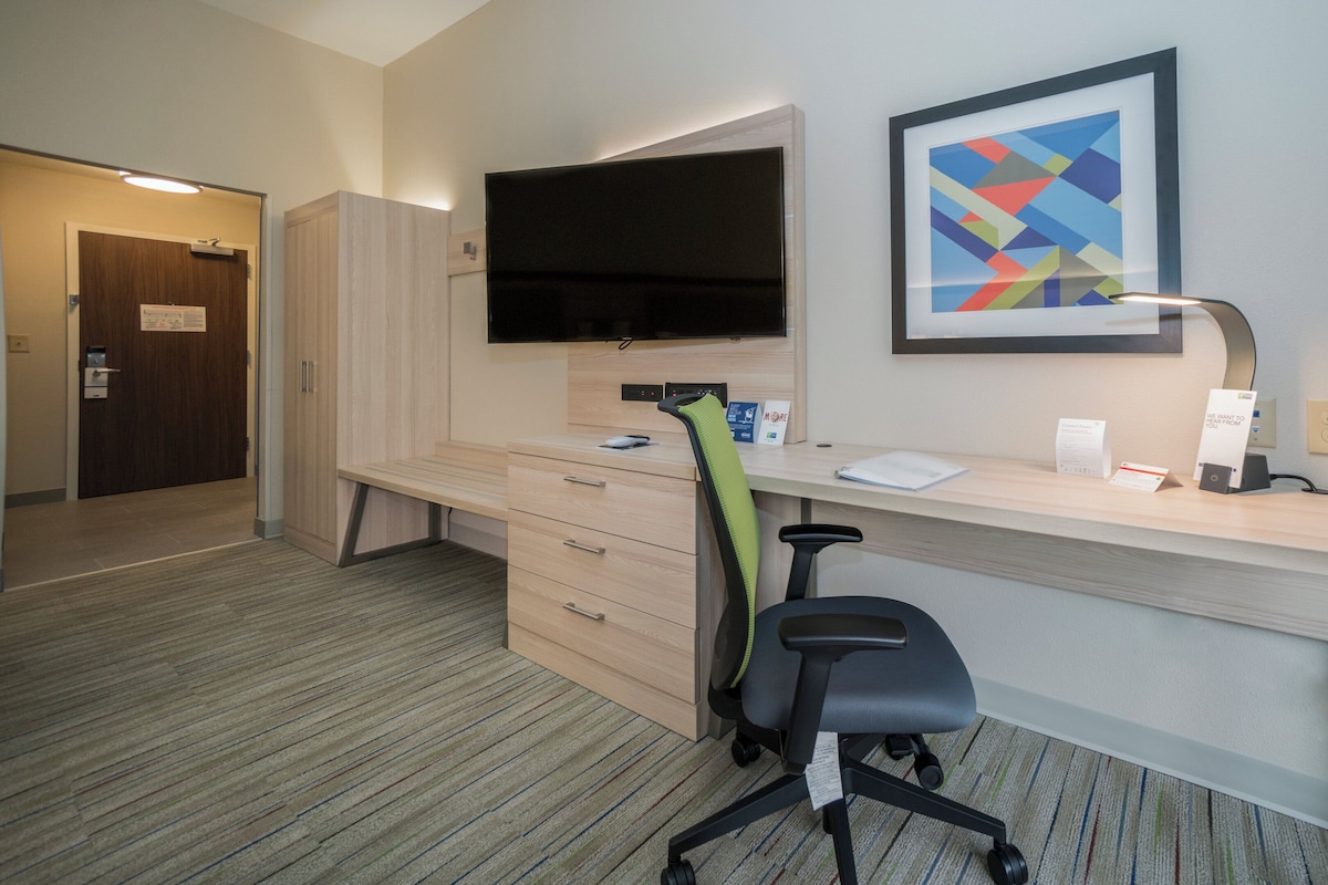 Quarto de hotel com escrivaninha, cadeira, televisão, obras de arte e uma porta.