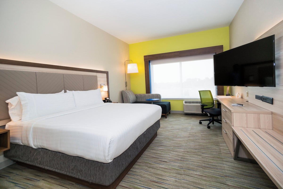 Quarto de hotel com cama, escrivaninha, cadeira, televisão e janela.