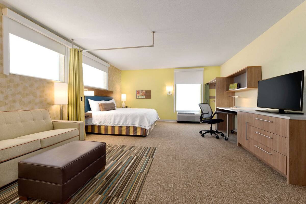 Een hotelkamer met een bed, een bank, een bureau met een televisie en een stoel.