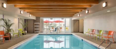 A swimming pool with a wooden ceiling, chairs, and a view of the outside.