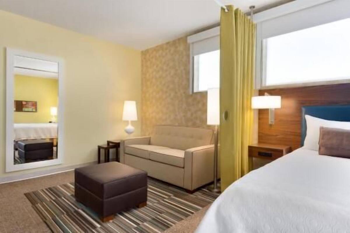 Een hotelkamer met een bed, een bank, een tafeltje, een lamp en een raam met gordijnen.