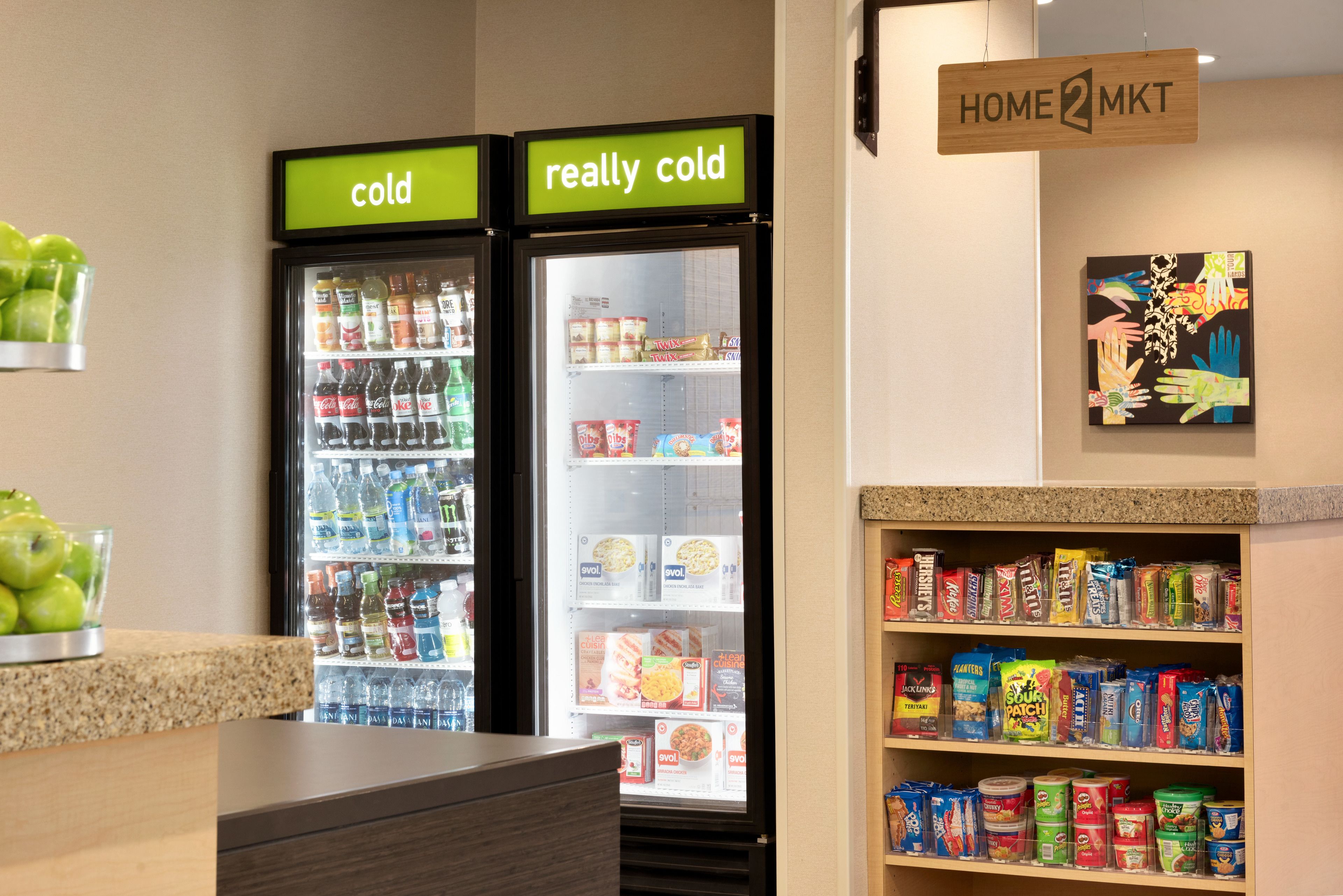 Una sección refrigerada con etiquetas que indican 'frío' y 'muy frío', una exhibición de conservas y un letrero que dice HOME2MKT.