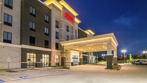 Entrada de hotel com placa visível, área de estacionamento coberta e símbolo de estacionamento para deficientes.