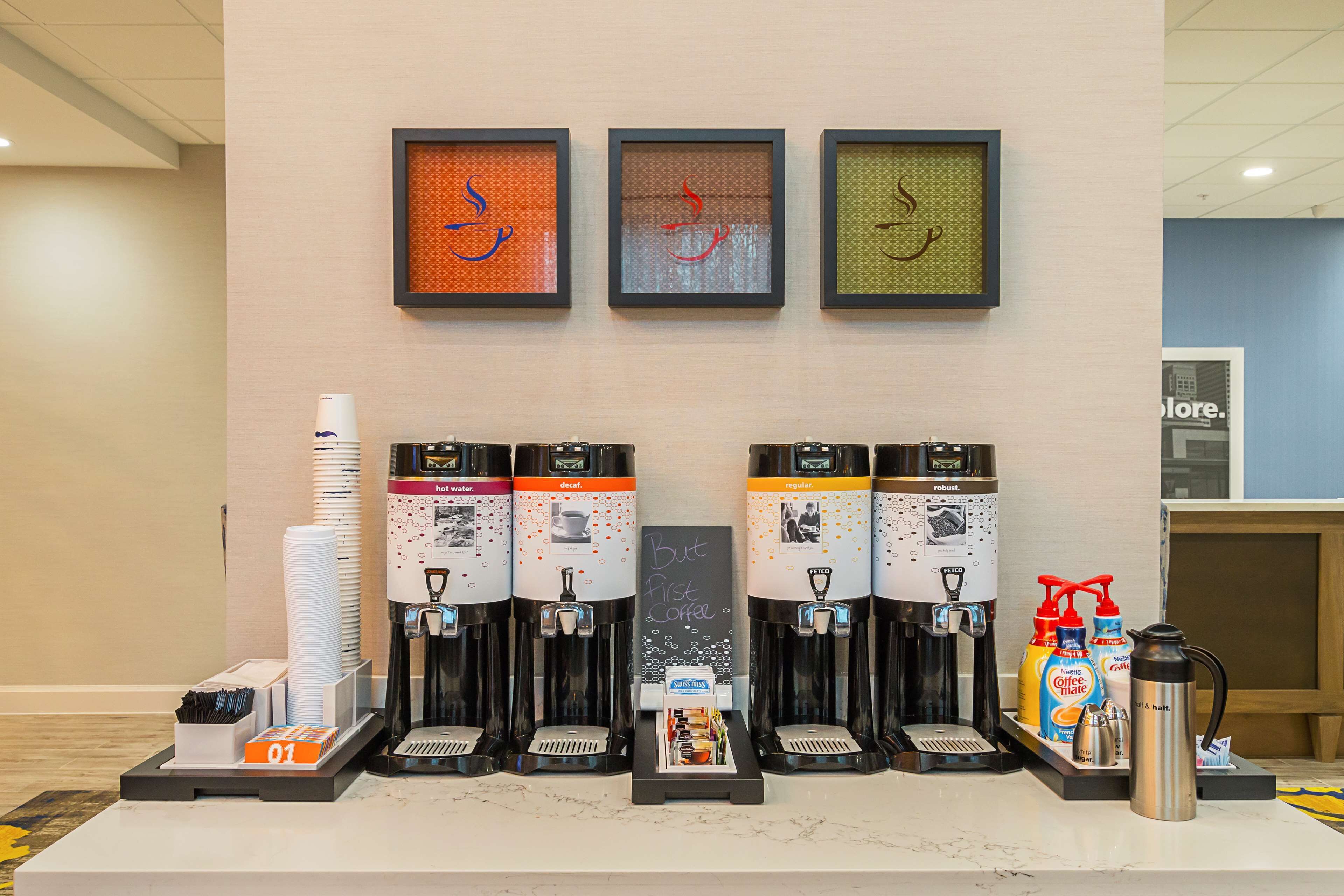 A coffee station with multiple dispensers, a chalkboard sign, and a coffee maker.