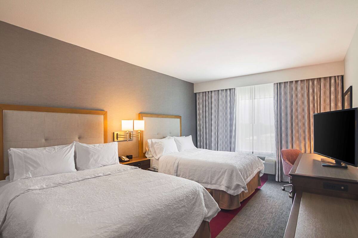 Habitación de hotel con dos camas, un escritorio, un televisor y una ventana con cortinas.