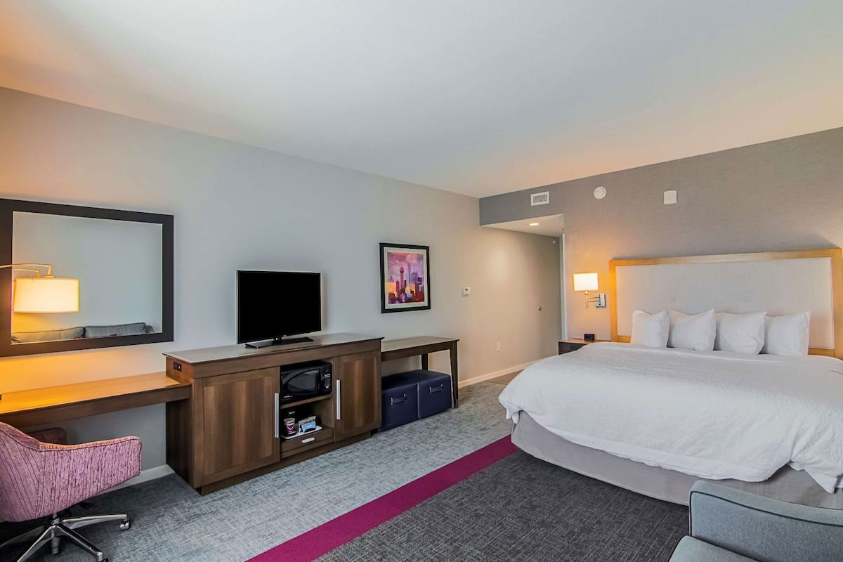 Una habitación de hotel con una cama, un escritorio con televisor, un microondas y una silla.