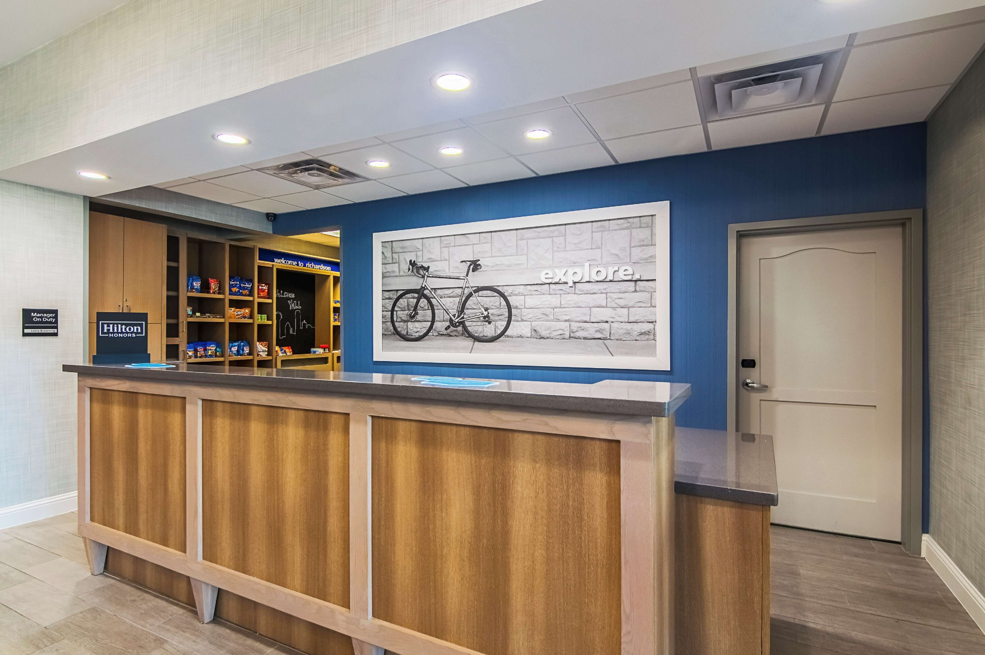 Un taulell de recepció d'hotel amb acabat de fusta, una paret blava amb un mural de temàtica ciclista i una porta tancada a la dreta.
