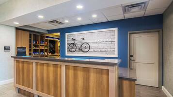 Un mostrador de recepción de hotel con detalles de madera, una pared azul con un mural con temática de bicicletas y una puerta cerrada a la derecha.