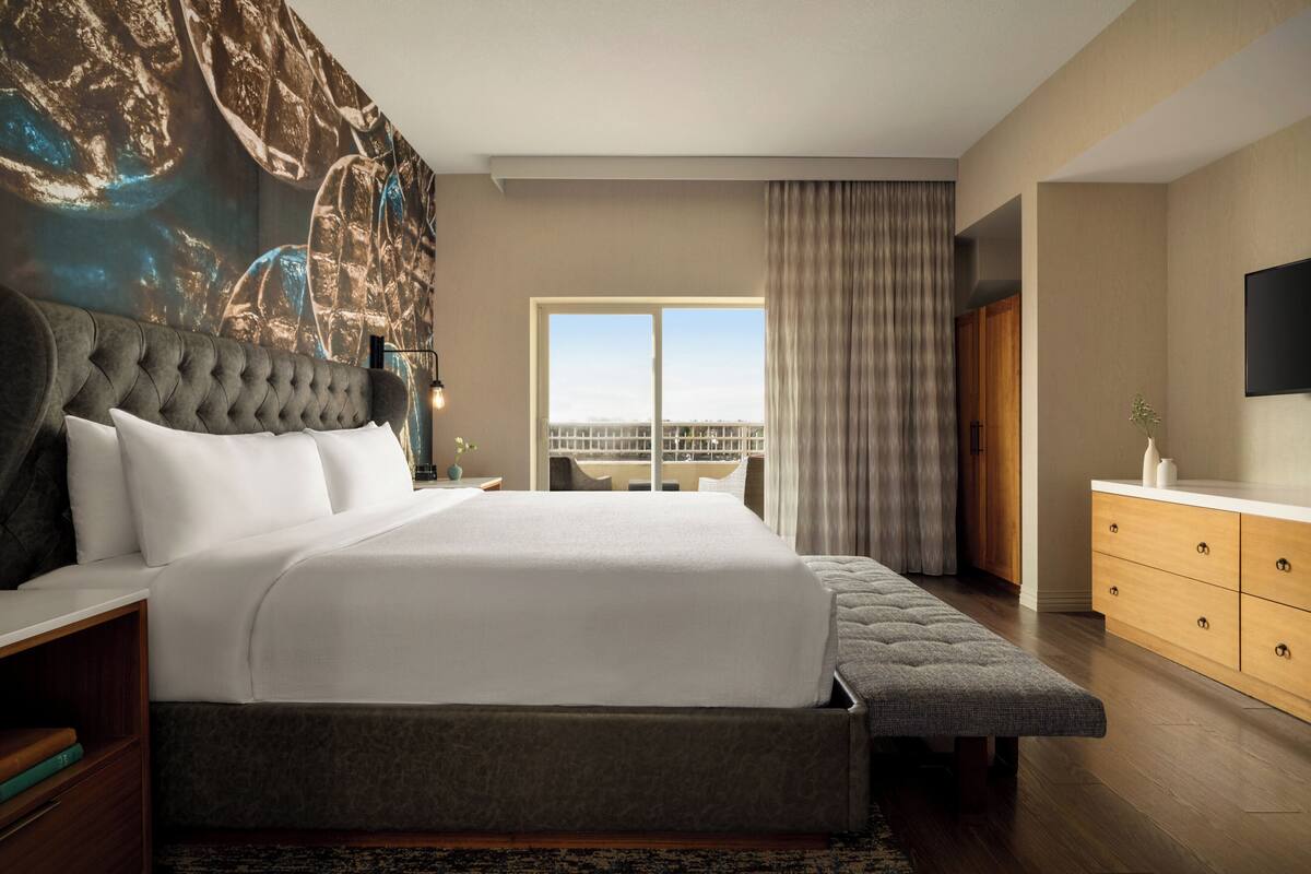 Une chambre d’hôtel moderne avec un grand lit, une vue sur la ville et une commode en bois.