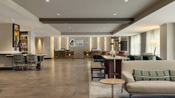 A spacious hotel lobby with a central reception desk, a bar area, and seating arrangements.