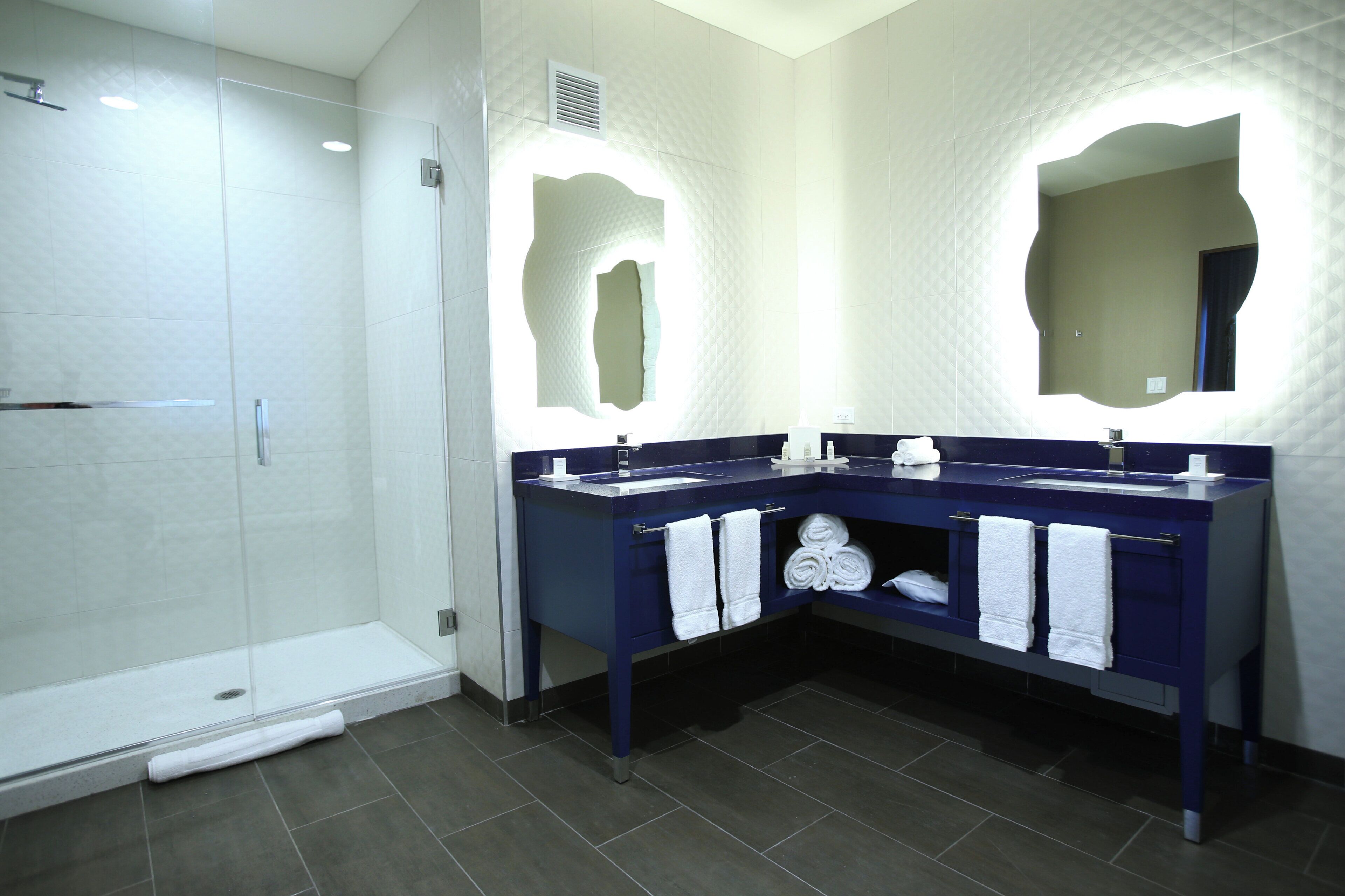 A modern bathroom with a walk-in shower, two sinks with mirrors, and a towel rack.