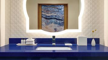 A bathroom with a blue countertop, a white sink, and a mirror with a framed artwork.
