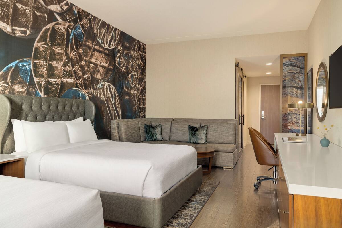 Une chambre d’hôtel moderne, dotée d’un grand lit, d’un canapé, d’un bureau et d’un grand tableau abstrait accroché au mur.