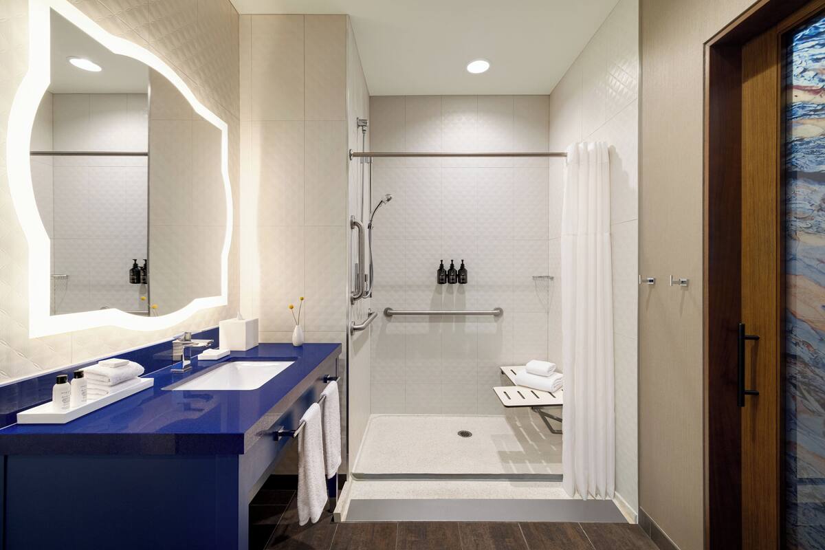 Une salle de bain moderne avec un meuble-lavabo bleu, un grand miroir, une douche avec une porte en verre et une porte en bois.