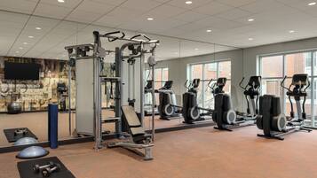 A gym with various exercise equipment, a large mirror, and windows with a view of the outside.