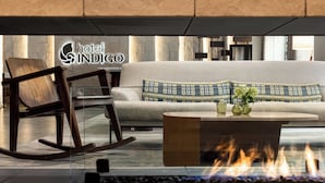 A modern hotel lobby with a sofa, a wooden rocking chair, a round coffee table, and a fire feature.