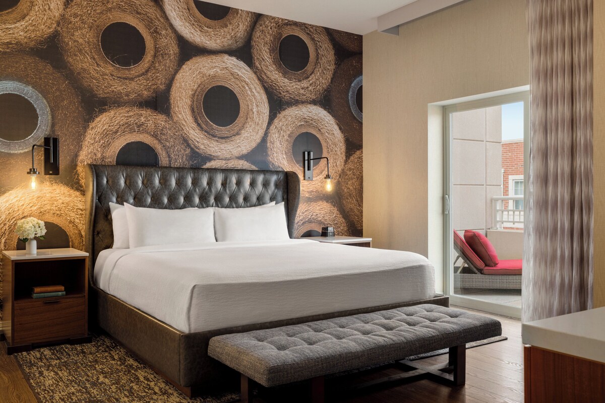 Une chambre d’hôtel avec un grand lit, un banc, une table de chevet, une lampe et un mur orné de motifs circulaires.