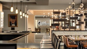 A modern hotel lobby with a long reception desk, leather seating, and a prominent 'hotel INDIGO' sign.