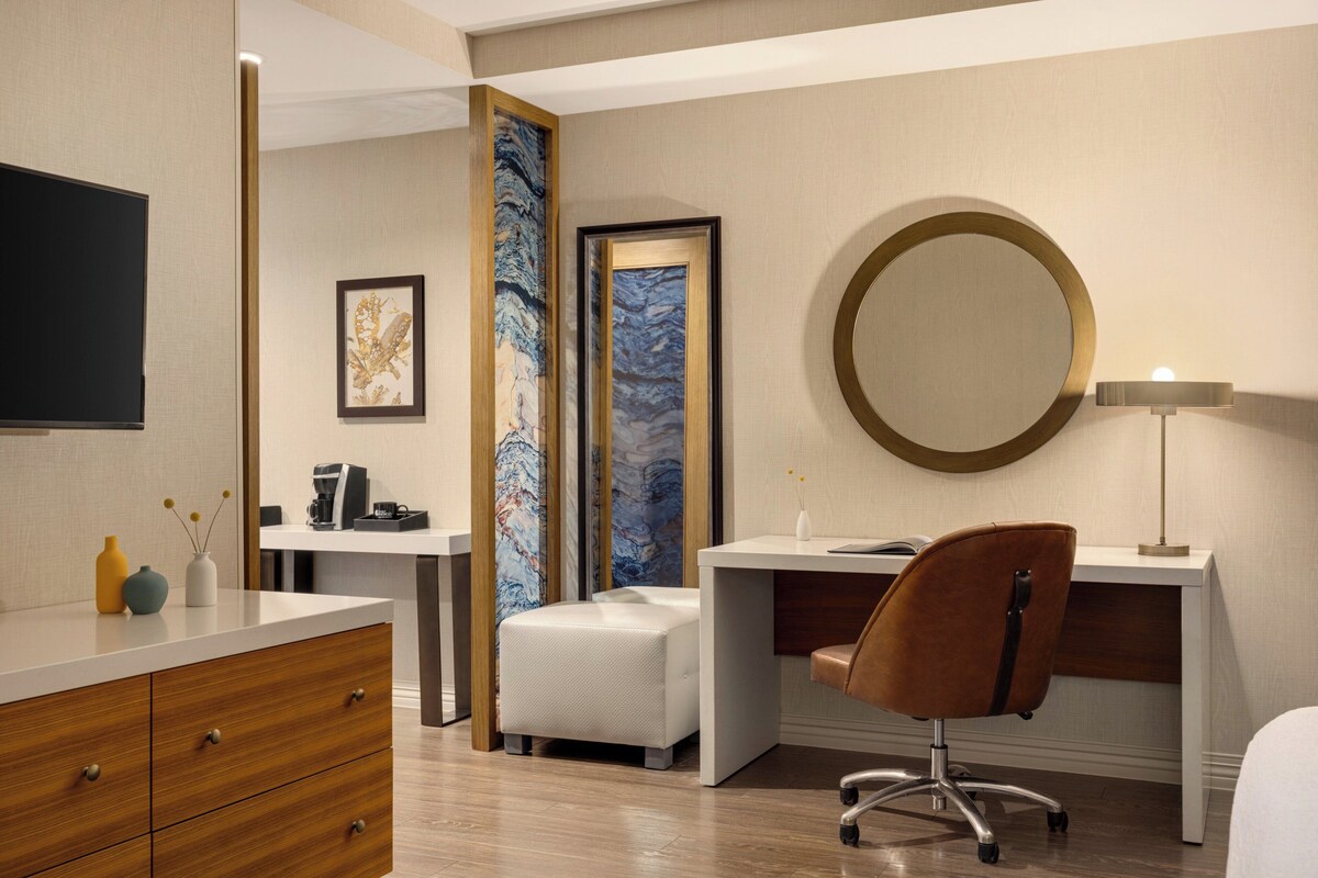 Une chambre d’hôtel moderne équipée d’un bureau, d’une chaise et d’un grand miroir.