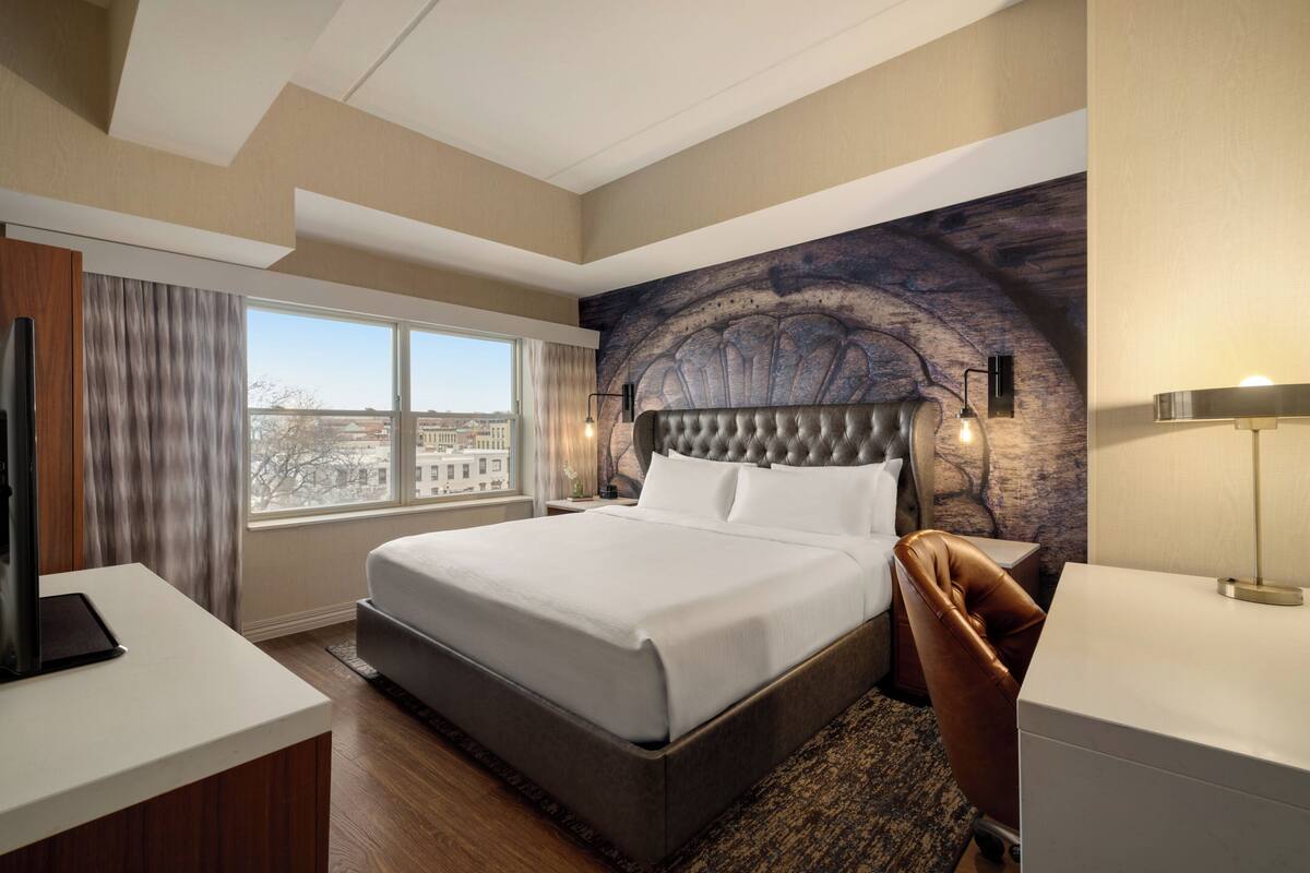Une chambre d’hôtel moderne avec un grand lit, un bureau, une chaise et une vue sur la ville.