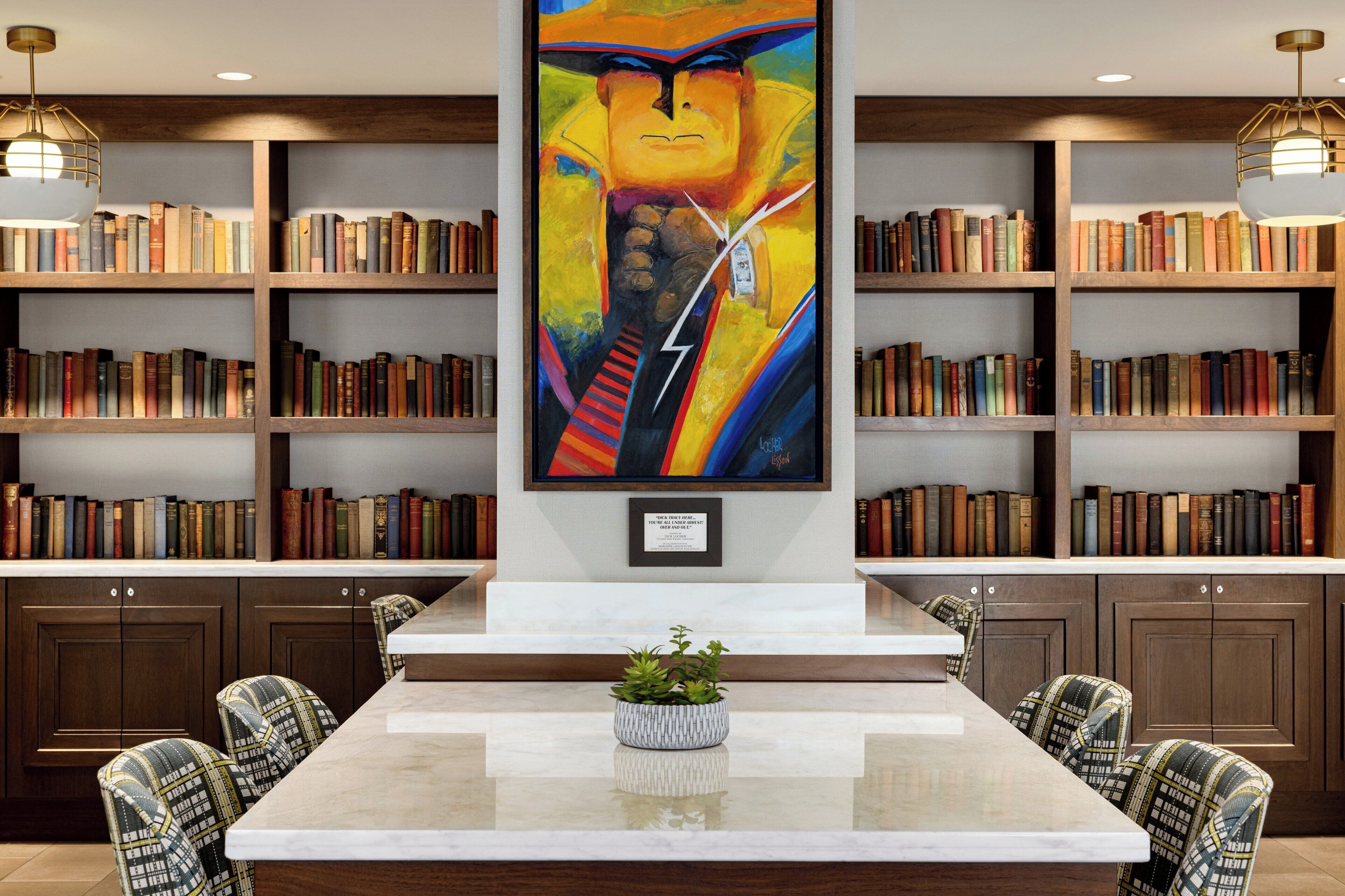 A library with bookshelves, a central painting, a marble table, and patterned chairs.