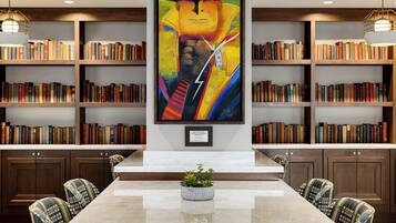 A library with bookshelves, a central painting, a marble table, and patterned chairs.