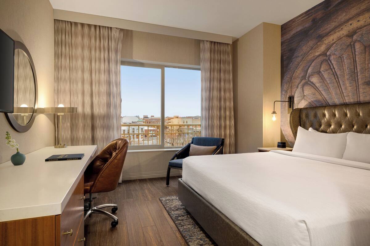 Une chambre d’hôtel avec un grand lit, un bureau avec une chaise, une télévision et une fenêtre avec des rideaux.