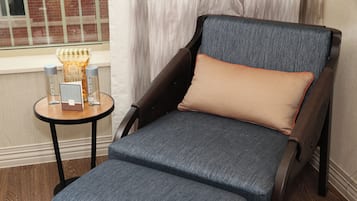 A dark brown leather armchair with a blue fabric seat and backrest, an orange cushion, and a small round table with two glass bottles and a box of tissues.