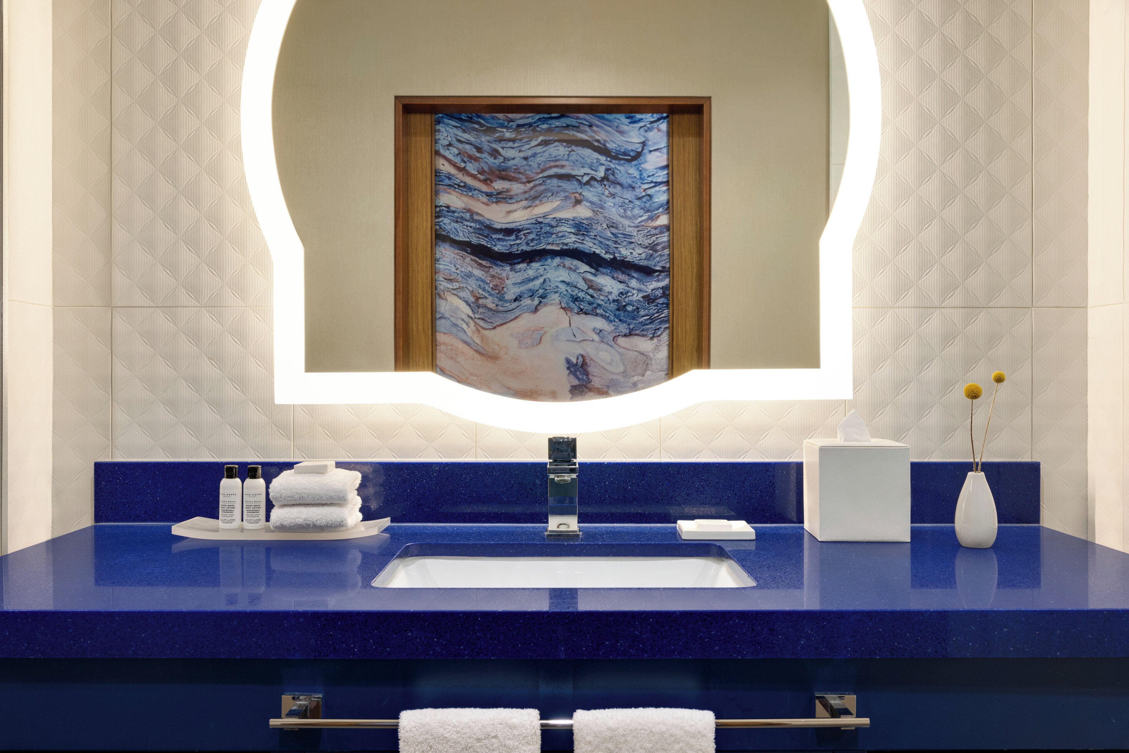 Un baño con encimera azul, un lavabo, un espejo y una obra de arte enmarcada sobre el espejo.