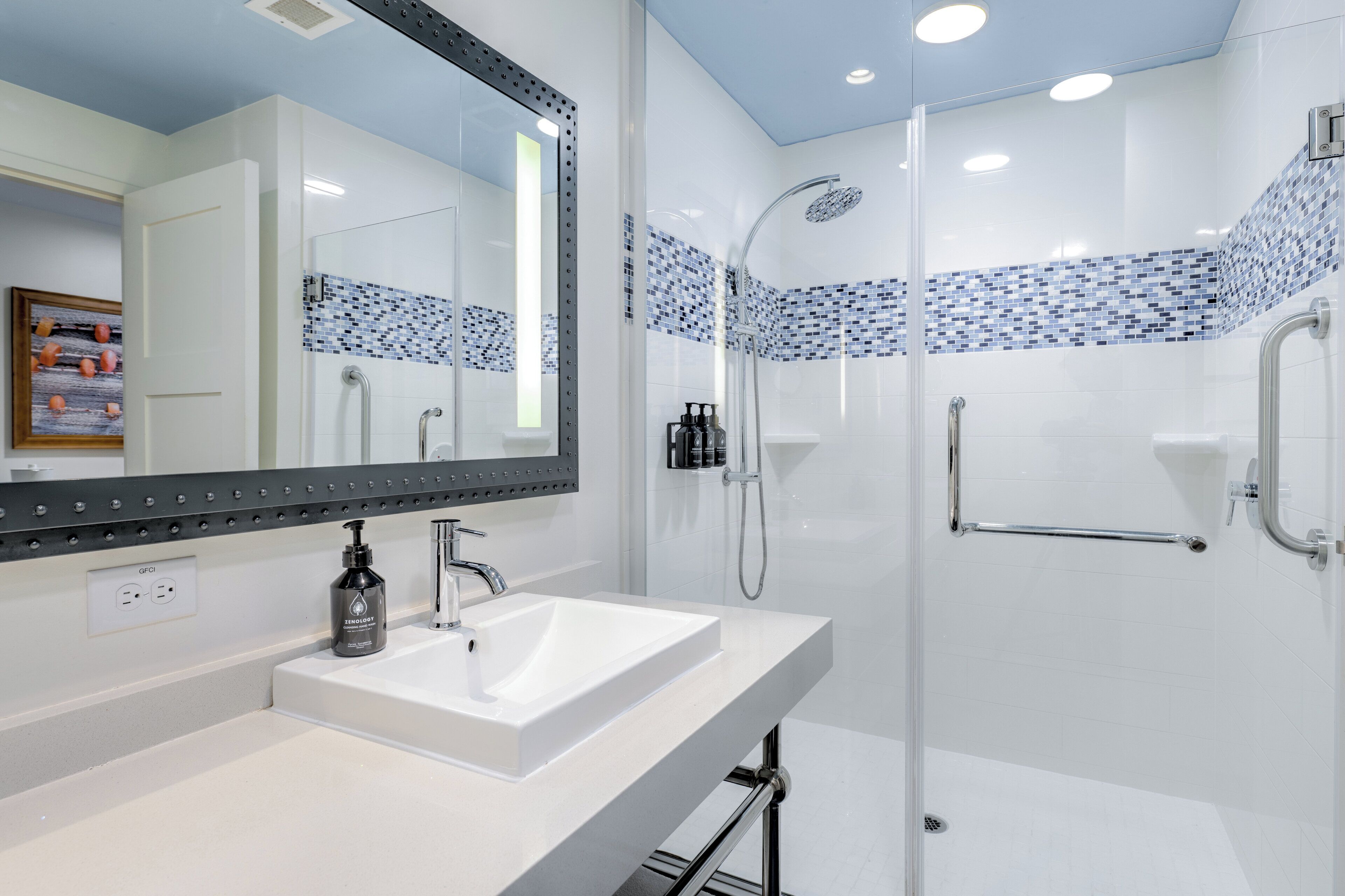 A modern bathroom with a white sink, a large mirror, and a glass-enclosed shower area.