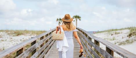 A wooden boardwalk leading to a beach with palm trees in the background.