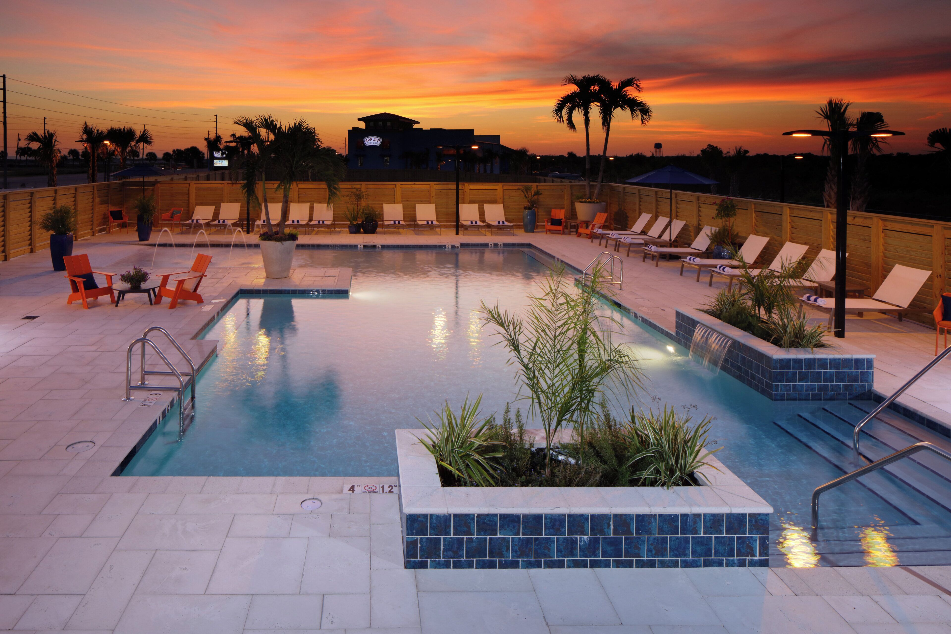 A pool area with lounge chairs and a view of the sunset.