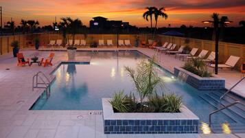 A pool area with lounge chairs and a view of the sunset.