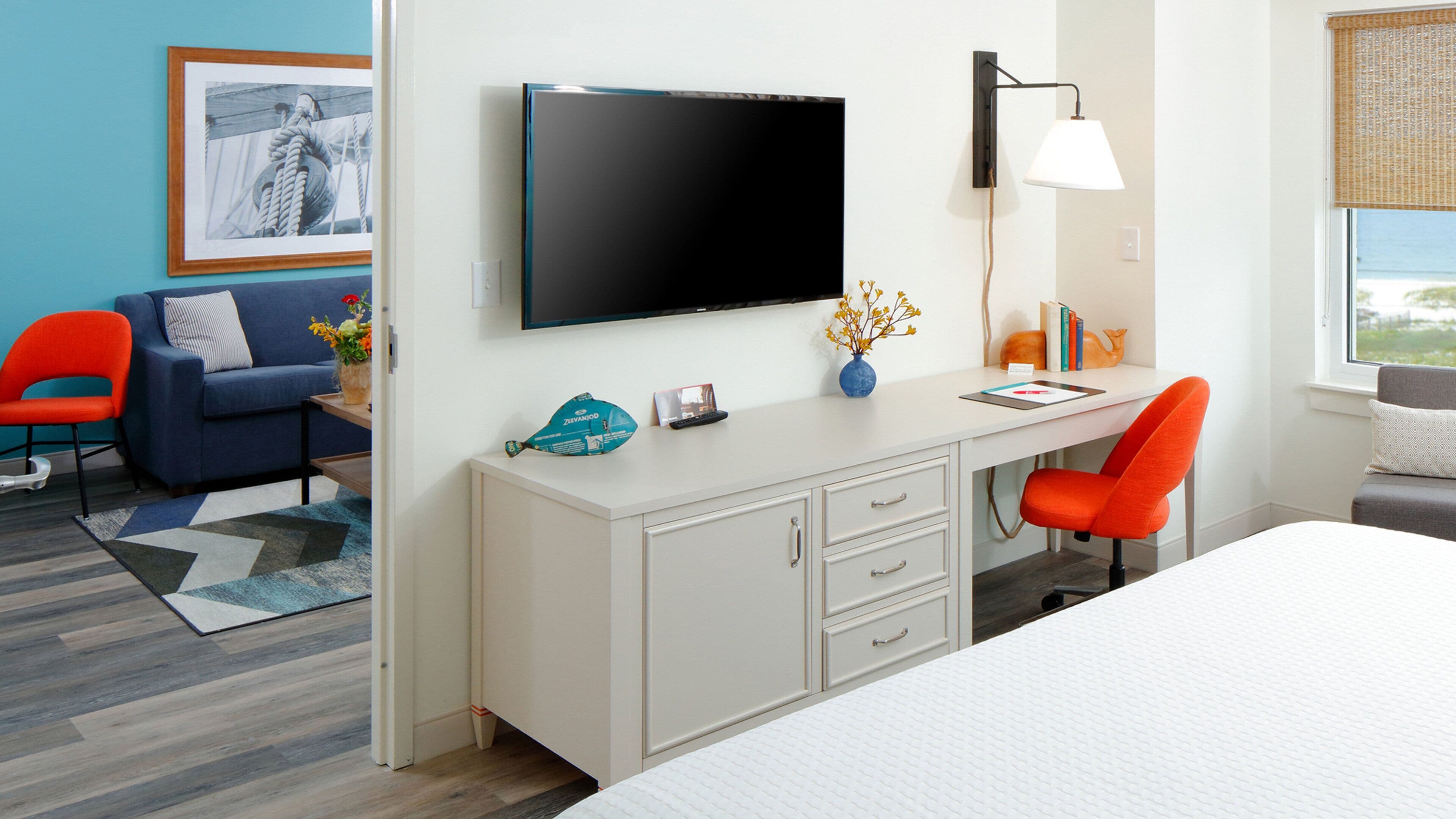 A hotel room with a bed, a desk with a chair, a television, a window with a view, and a framed picture on the wall.