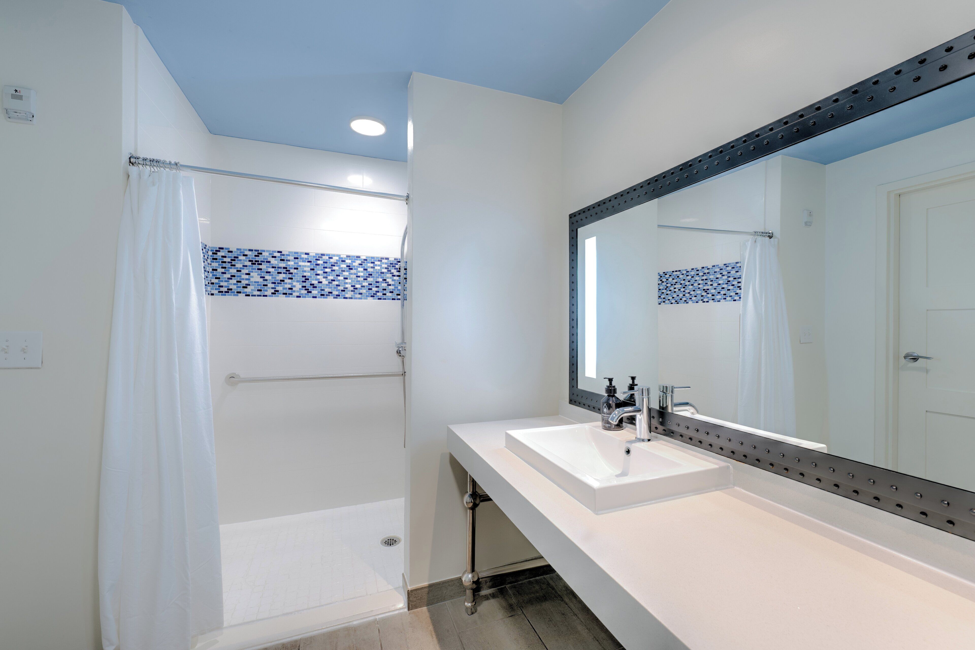 A modern bathroom with a white sink, a large mirror, and a shower area.