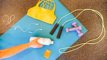 A blue exercise mat with a yellow bag, pink dumbbells, a jump rope, and a bottle of lotion.