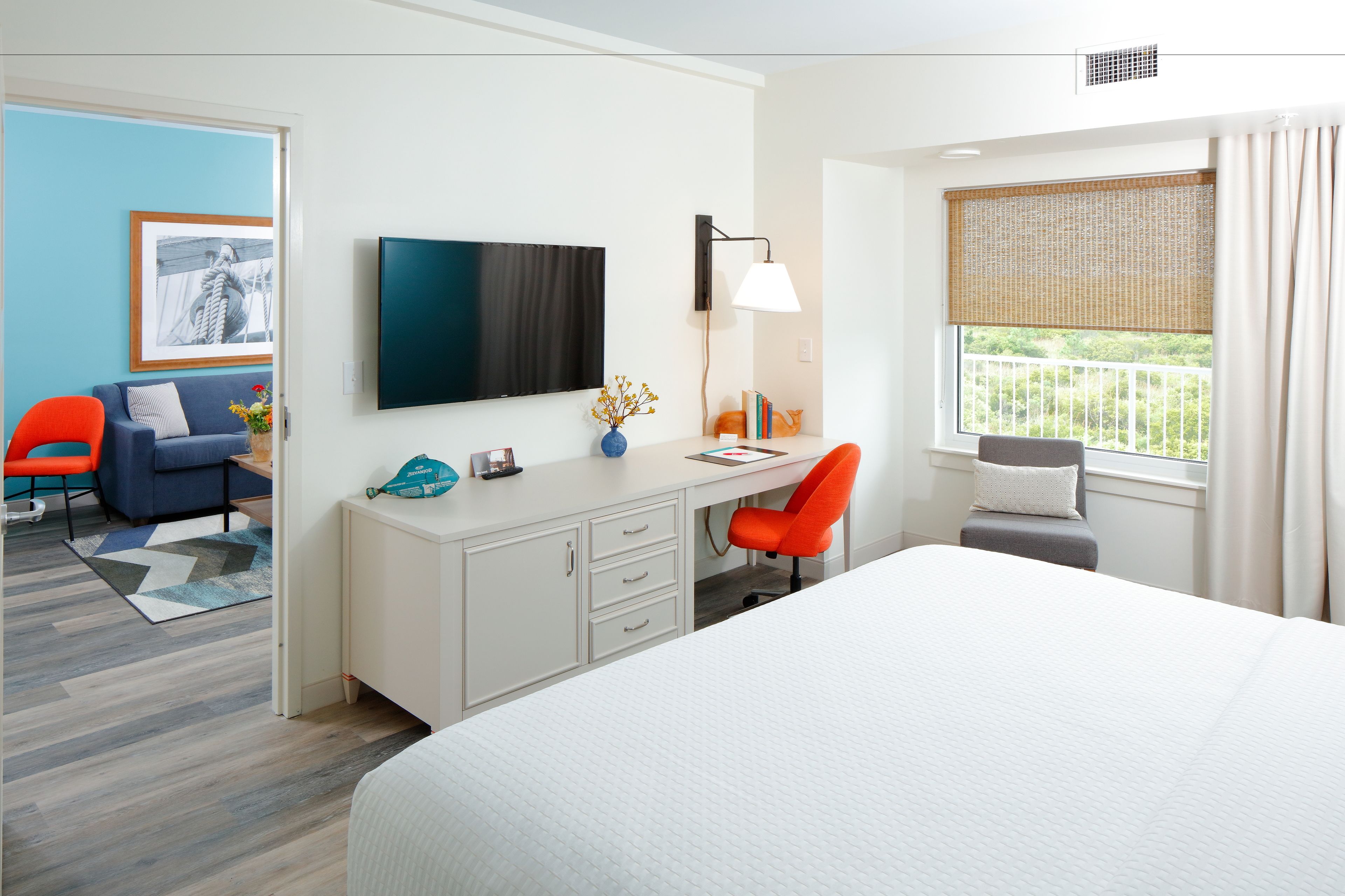 Una habitación de hotel moderna con una cama grande, un escritorio con computadora, un televisor y un balcón con vistas.