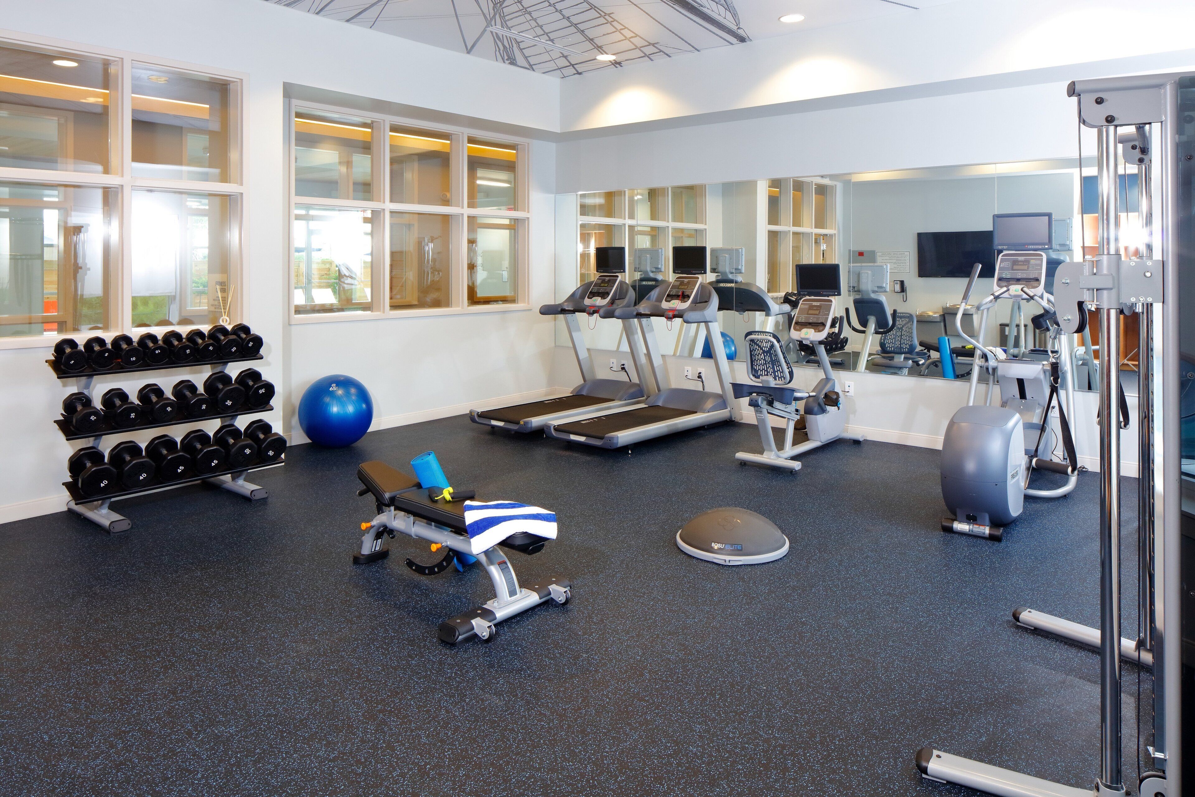 Une salle de sport équipée de tapis de course, de vélos elliptiques, d’un rameur, d’haltères et d’un ballon d’exercice bleu.