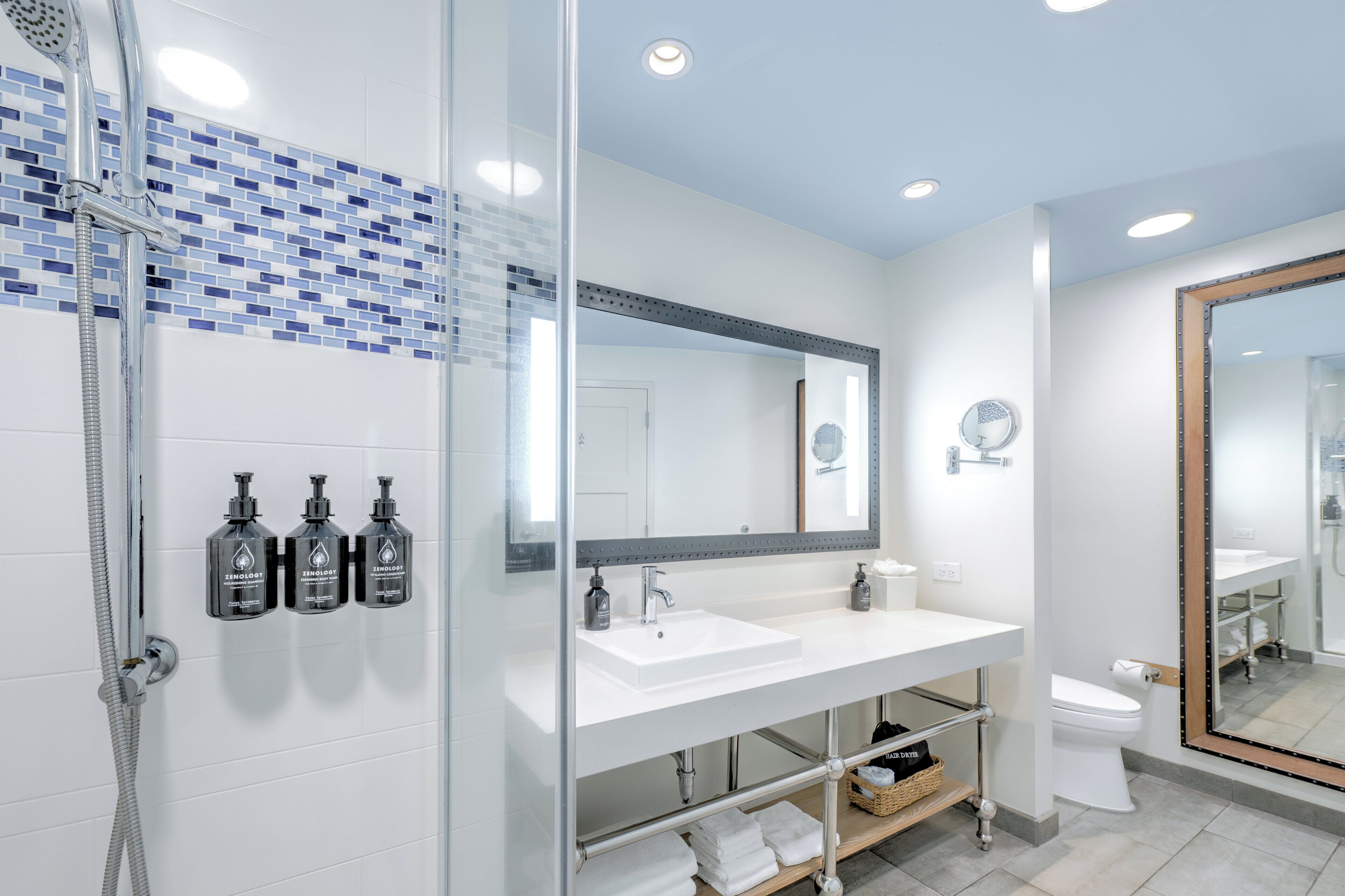 Un baño moderno con cabina de ducha de vidrio, lavabo blanco y un espejo grande.