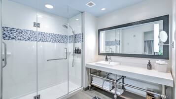 Un baño moderno con cabina de ducha de vidrio, un lavamanos blanco con un espejo grande y un salpicadero de azulejos.