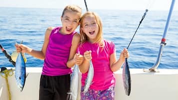 Two individuals holding fish on a boat with the ocean in the background.