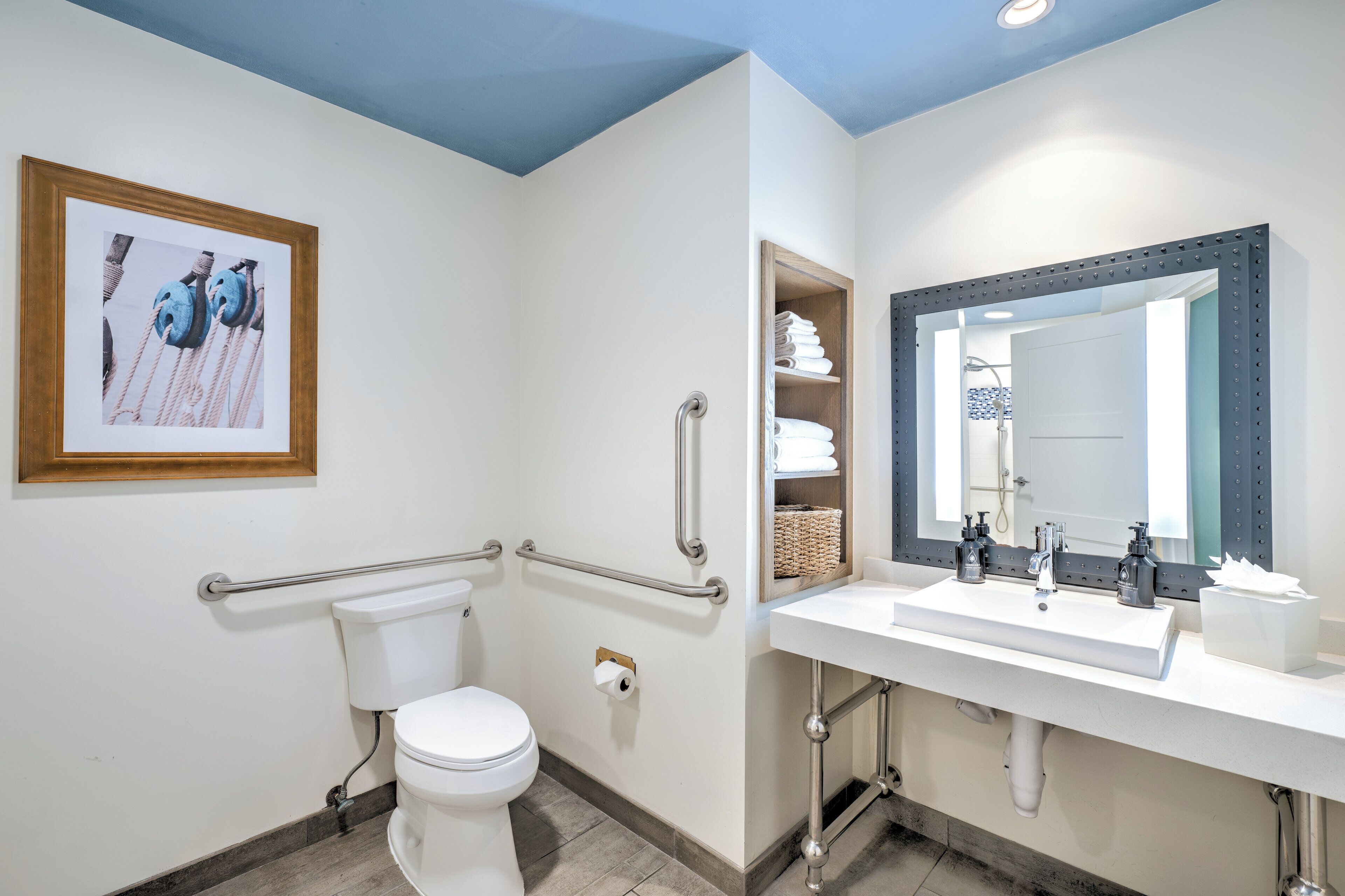 A modern bathroom with a white toilet, a sink with a mirror, and a framed picture on the wall.