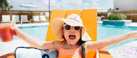 Un enfant assis sur une chaise au bord de la piscine, les bras tendus, tenant une boisson.