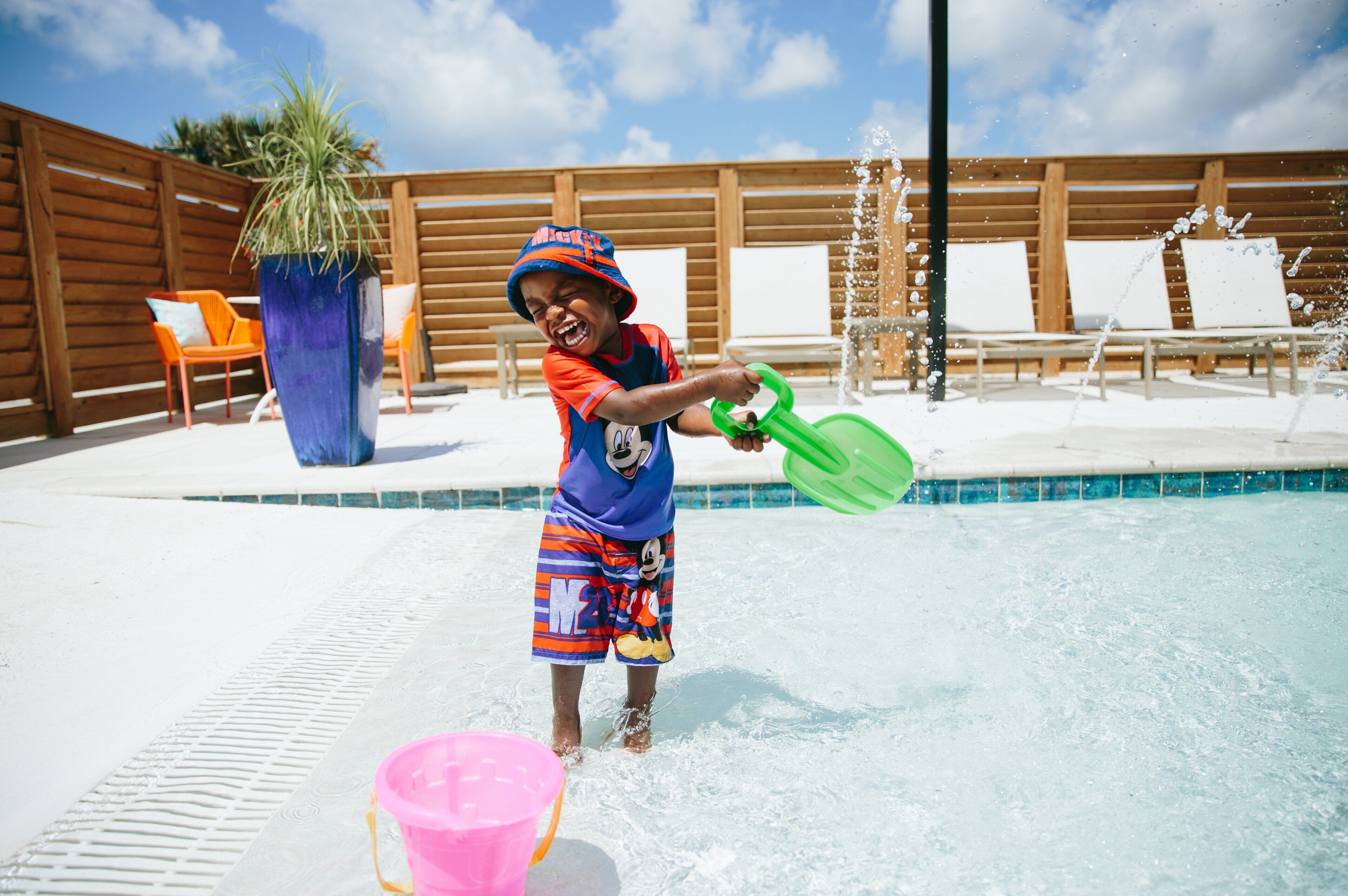 A child playing in a pool with a green shovel and a pink bucket.
